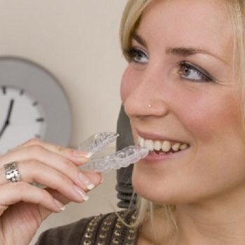 A woman with blonde hair holding an Invisalign aligner in front of her mouth