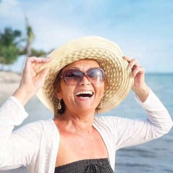 Smiling, happy woman on the beach wearing a hat and sunglasses