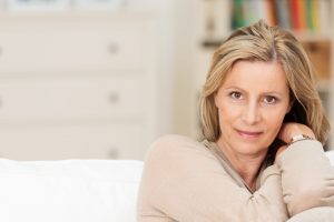 A middle aged woman leaning against the side of the couch slightly smiling