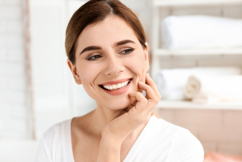 A middle aged woman with her hand on her face and smiling