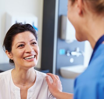 A doctor with her hand on her patients should while the patient is smiling